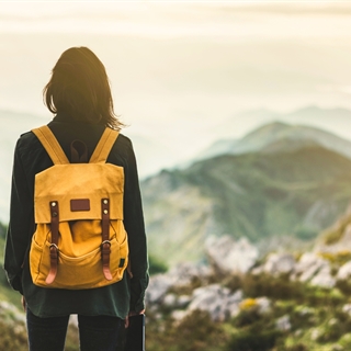 woman with a yellow backpack looking out at the mountains