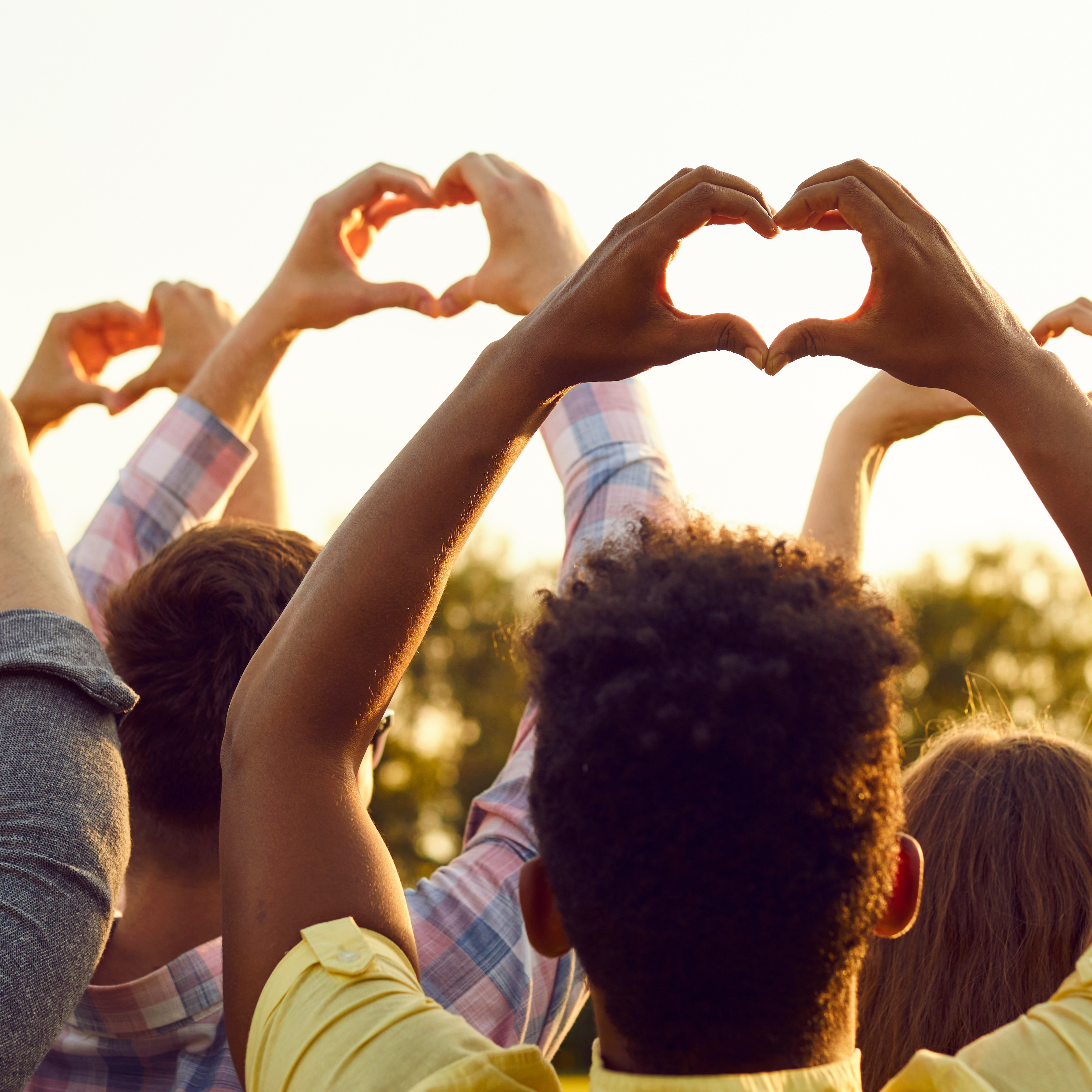 Group of people with arms raised making the shape of a heart with their hands